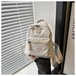 Detail of a beige mini nylon backpack with zipper pockets and durable woven texture