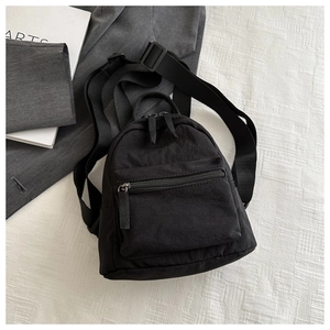 Flat lay of a black mini nylon backpack with zipper front pocket on white fabric