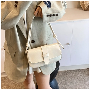 Detail of minimalist cream rectangular shoulder bag showing crossbody strap with knot details