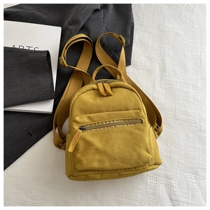 Detail of a ginger yellow mini canvas backpack with a front zipper pocket and adjustable straps