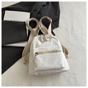 Detail of a minimalist cream white canvas backpack featuring textured fabric and front pocket