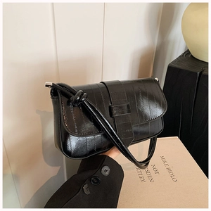 Close-up of black glossy leather shoulder bag with vertical texture and buckle strap detail