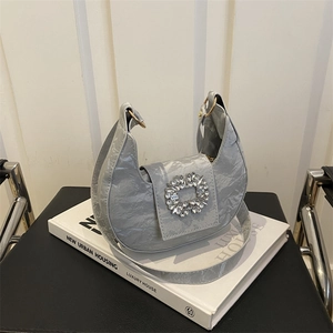 Silver pleated crescent bag with a sparkling rhinestone buckle on stacked white books