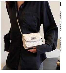 Detail of white quilted crossbody bag with metal chain strap on black satin shirt