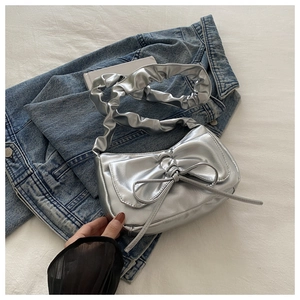 Detail of silver metallic cloud bag with bow accent on denim jacket background