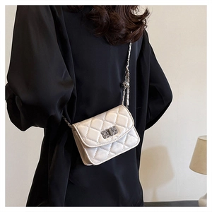Close-up of white quilted crossbody bag with metal chain strap on a black outfit