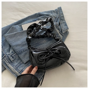 Detail of glossy black patent leather shoulder bag with bow and scrunchie strap