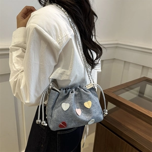 Light blue denim drawstring bucket bag featuring colorful heart patches and silver chain strap