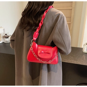 Detail of red underarm bag featuring a woven strap and delicate floral metal chain accent