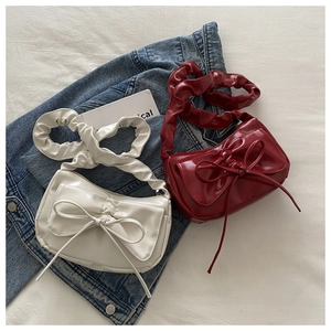 Close-up of white and burgundy glossy faux leather handbags with bow and pleated handle
