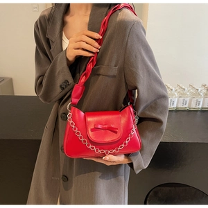 Detail of red leather shoulder bag with bow, flower chain, and twisted shoulder strap