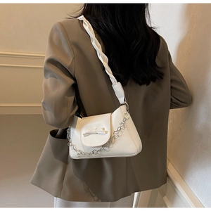 Detailed view of white shoulder bag with bow decor and floral chain on female model