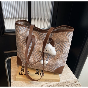 Detailed view of large tote bag with textured fabric, leather straps and plush charm