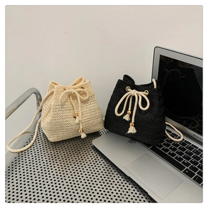 Detail showing woven texture and hemp rope handles on straw bucket bags in cream and black