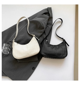 Close-up of stylish black and white quilted shoulder bags on a grey suit jacket background