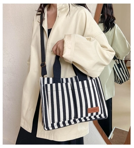 Detail of striped canvas tote bag with black handles, adjustable strap and fashion patch