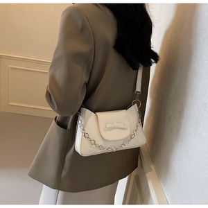 Close-up of a white bow shoulder bag with a unique silver floral metal chain strap
