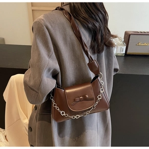 Detail of dark brown glossy leather shoulder bag featuring a decorative bow and flower chain