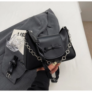 Detail of black matte leather handbag with bow decor and floral chain on a grey suit