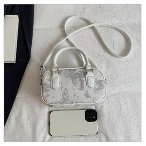 Mini cream pillow bag with butterfly print and shoulder strap shown with phone for scale