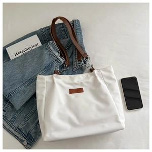 Top view of a large white tote bag with brown leather handles and silver chain detail
