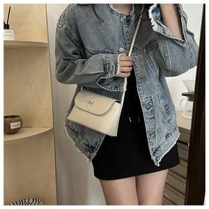 Detail of cream shoulder bag with metal bow accent worn with denim jacket
