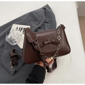Detail of dark brown shoulder bag with bow knot and floral silver chain strap