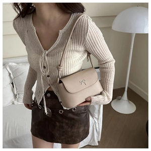 Detail of cream leather crossbody bag with silver bow buckle worn by model