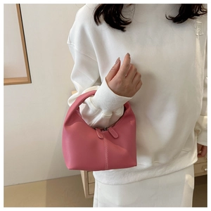 Close-up of a pink mini crescent handbag with dual zippers held by a model in white outfit