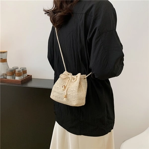 Minimalist cream woven bucket bag with drawstring closure and slim chain shoulder strap