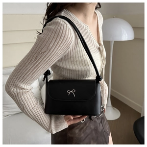 Detail of black matte leather shoulder bag featuring a silver metal bow and knotted strap