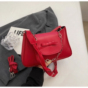 Detail of red faux leather handbag with bow ornament and clover metal chain strap