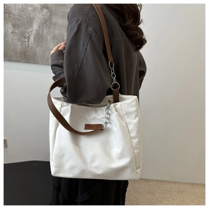Detail of white tote bag with brown leather strap and decorative silver chain on shoulder