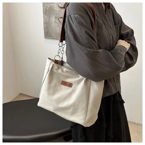 Detail of off-white nylon tote bag with leather chain strap on model for daily commute