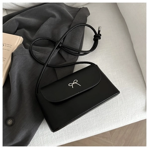 Detail of a matte black crossbody bag featuring a silver metal butterfly bow on the flap