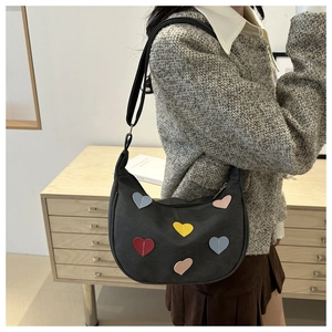Model wearing a black crescent shoulder bag with colorful embroidered hearts