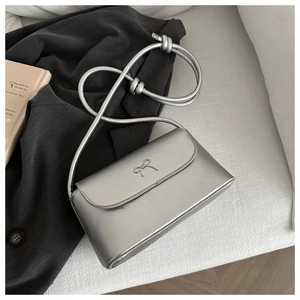 Detail of silver square bag featuring metallic texture and a bow-knot metal ornament
