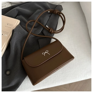 Close-up of deep brown crossbody bag with silver butterfly buckle on grey suit