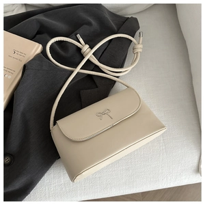 Detail of a creamy white leather crossbody bag featuring a silver metal butterfly ornament