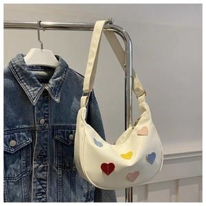 Close-up of white crescent shoulder bag featuring colorful heart-shaped stitched patches