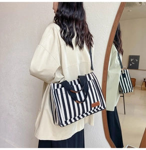 Side view of striped canvas tote bag with black strap and leather logo patch details