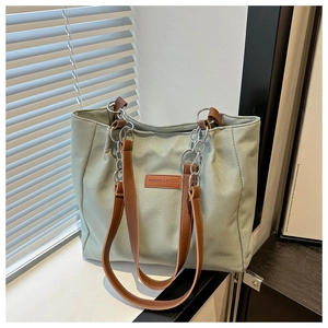 Detail of canvas tote bag with brown leather handles and silver metal chain links