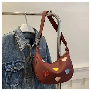 Detail of burgundy hobo bag featuring colorful heart patches on a denim jacket background