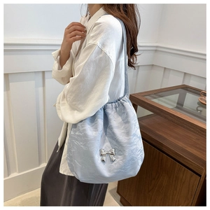 Detail of light blue pleated tote bag with a silver butterfly charm on a shoulder strap
