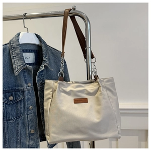 Detail of off-white tote bag featuring dark brown leather straps and silver metal chain link