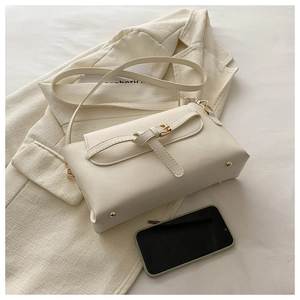 Detailed view of beige crossbody bag featuring gold hardware on a cream blazer