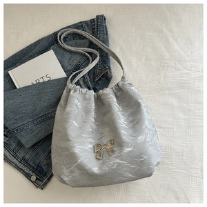 Detail of silver drawstring bucket bag with crinkled texture and metal bow ornament