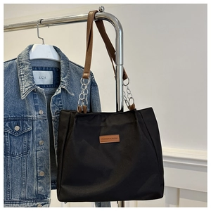 Detail of large black tote bag featuring brown leather straps and silver chain accents