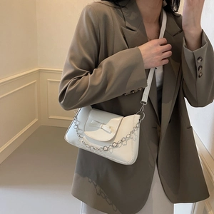 White leather crossbody bag with chain and bow detail worn by a model in a French setting
