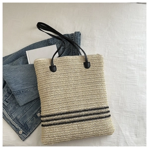 Détail d'un sac cabas en paille avec rayures noires et longues bandoulières